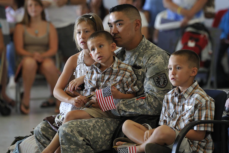 A man wearing a military uniform sits and holds a small boy on his lap, while a girl and boy sit close to him.