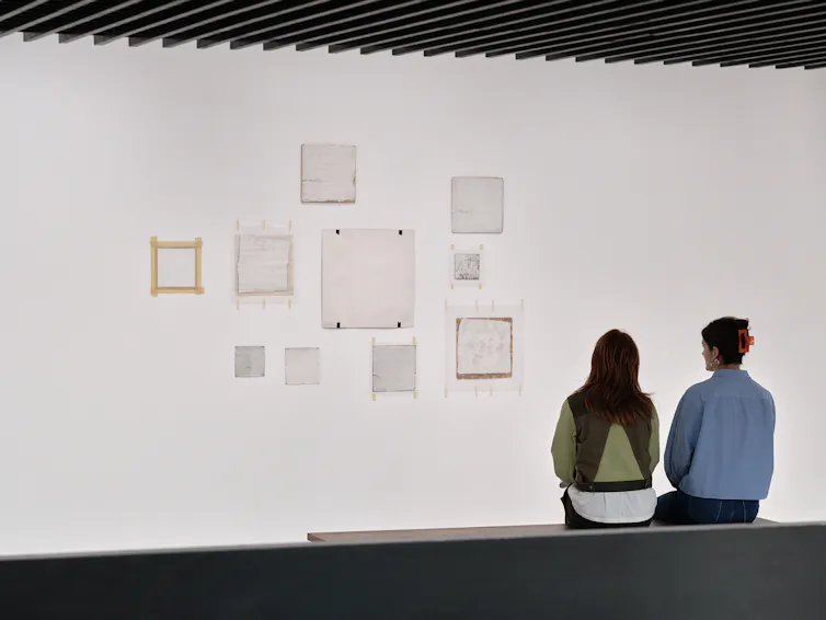 Two women looking at artworks taped to a gallery wall