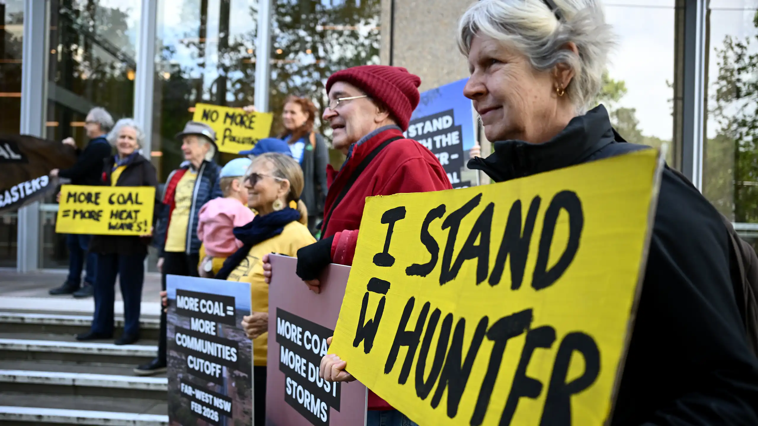 Community members stand outside the High Court of Australia in Sydney, holding placards about coal mining.