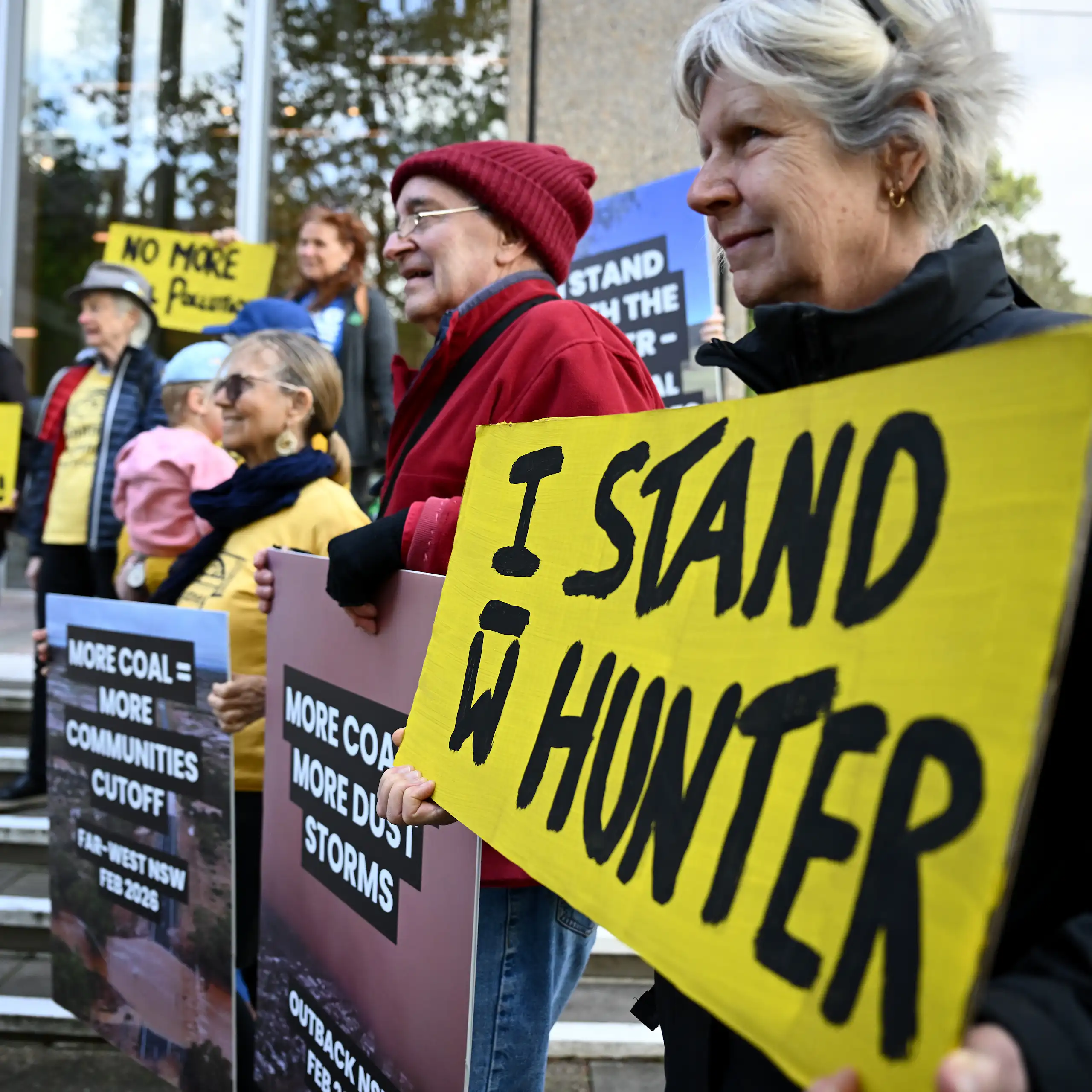 Community members stand outside the High Court of Australia in Sydney, holding placards about coal mining.
