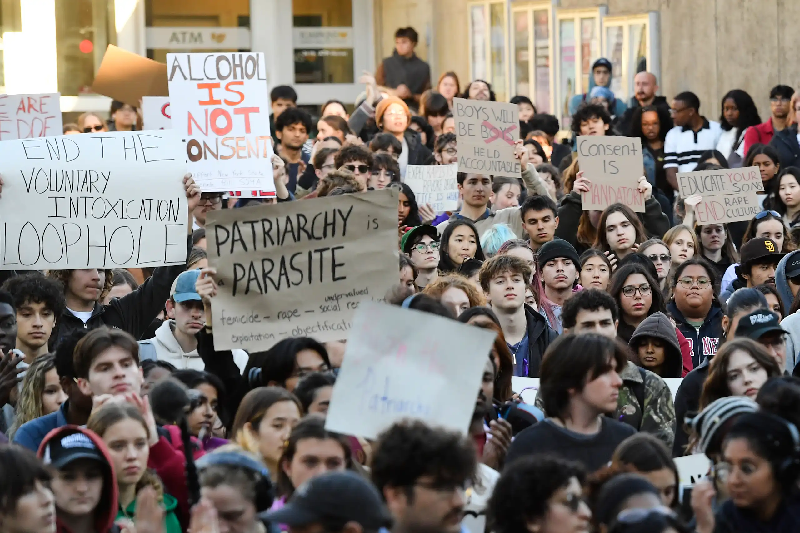 A crowd of students hold up protest signs. One reads 'alcohol is not consent.'