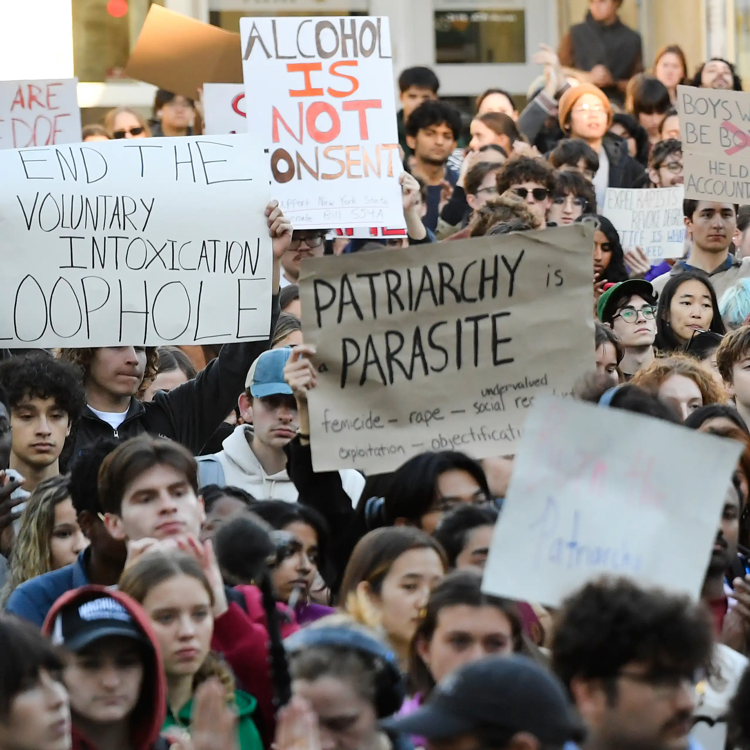 A crowd of students hold up protest signs. One reads 'alcohol is not consent.'