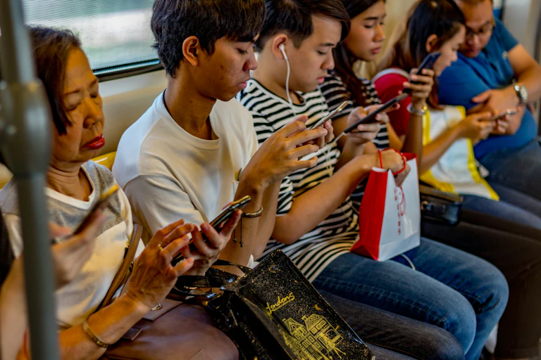 A culturally diverse group of people using phones, sat on a bench in a row