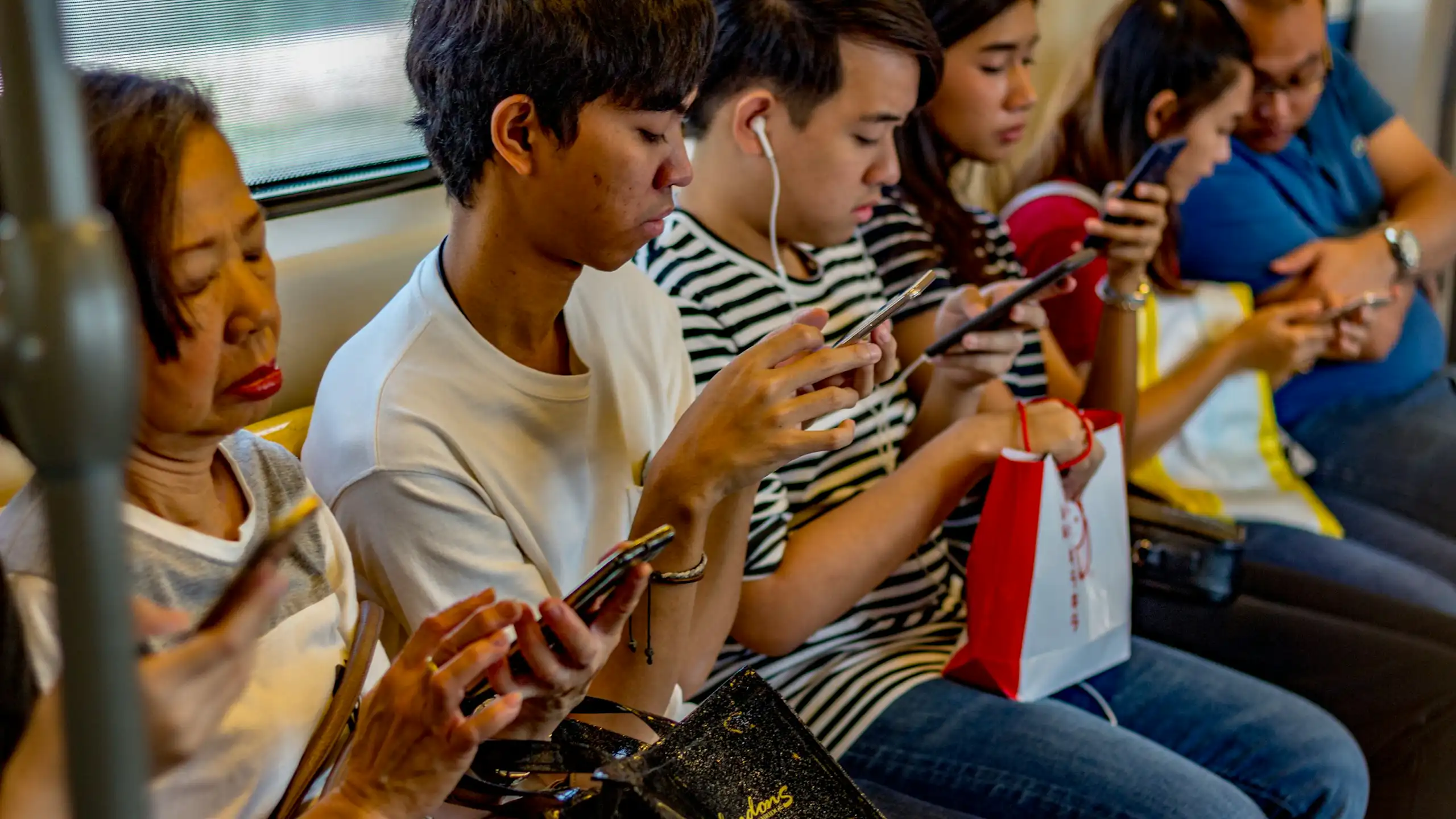 A culturally diverse group of people using phones, sat on a bench in a row