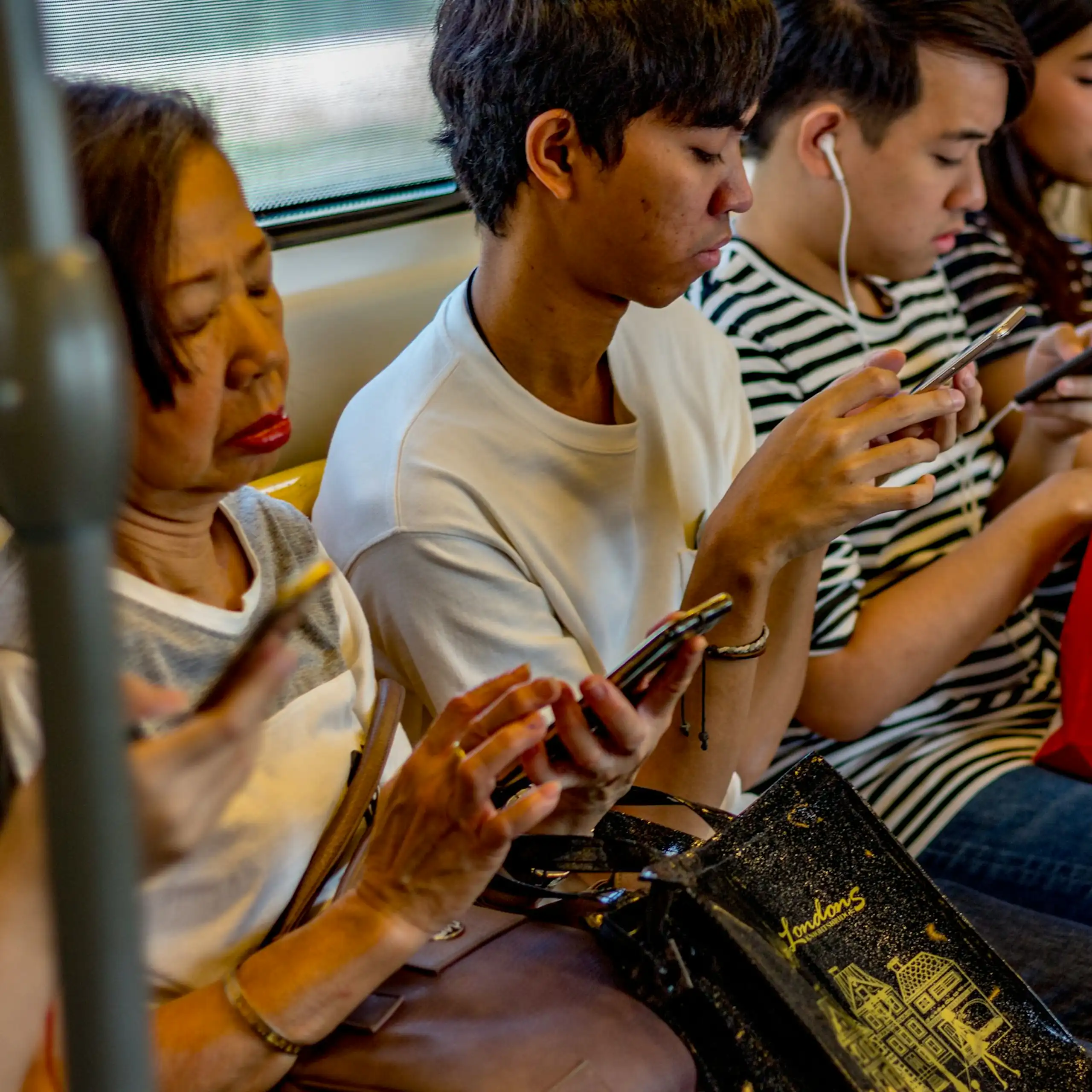A culturally diverse group of people using phones, sat on a bench in a row