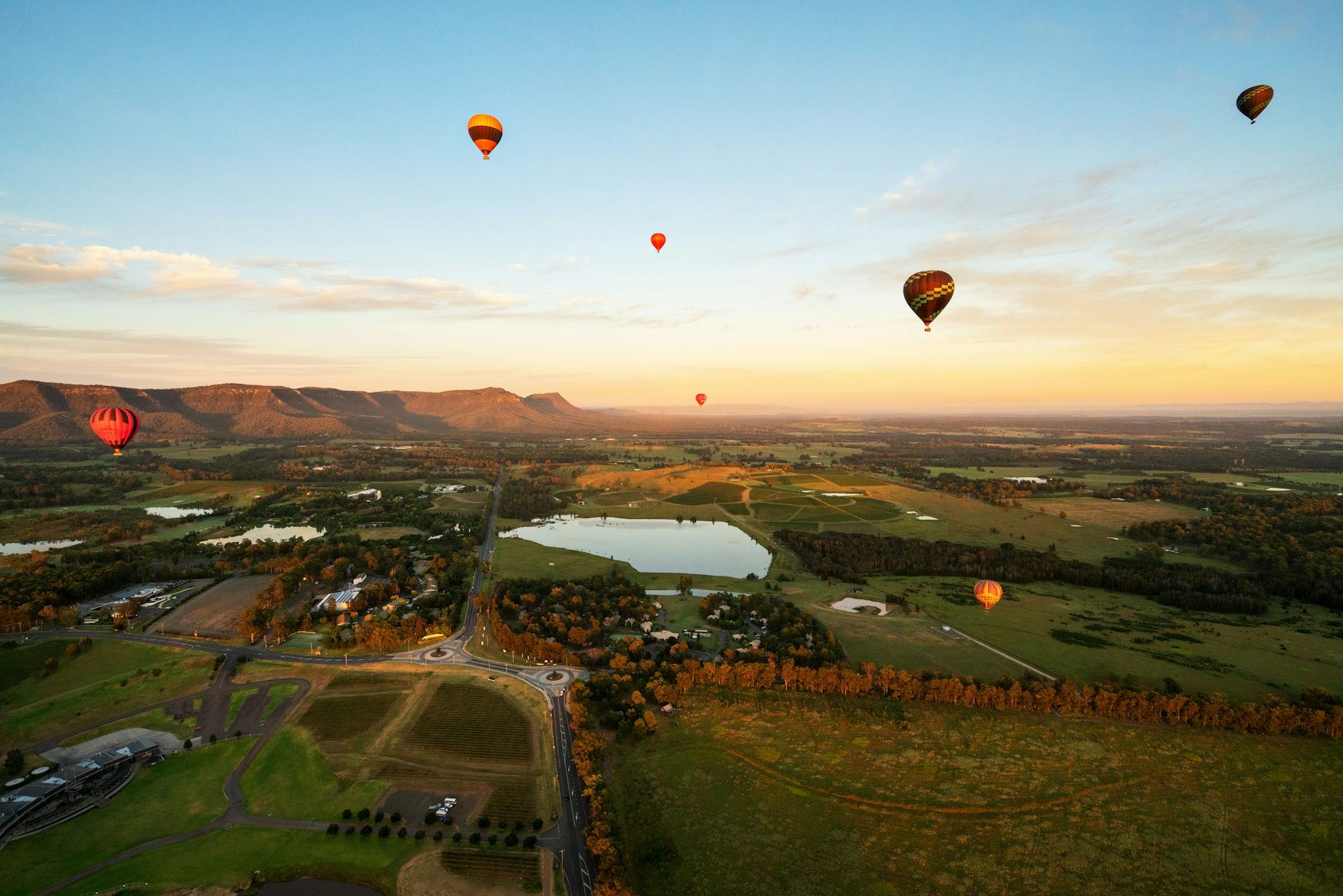 Hot air balloons float over a lush, green valley at sunrise.