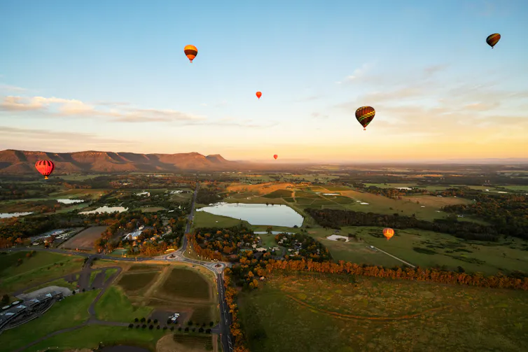 Hot air balloons float over a lush, green valley at sunrise.