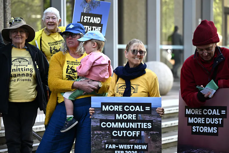 Community members gather outside the High Court of Australia, holding placards about coal mine.