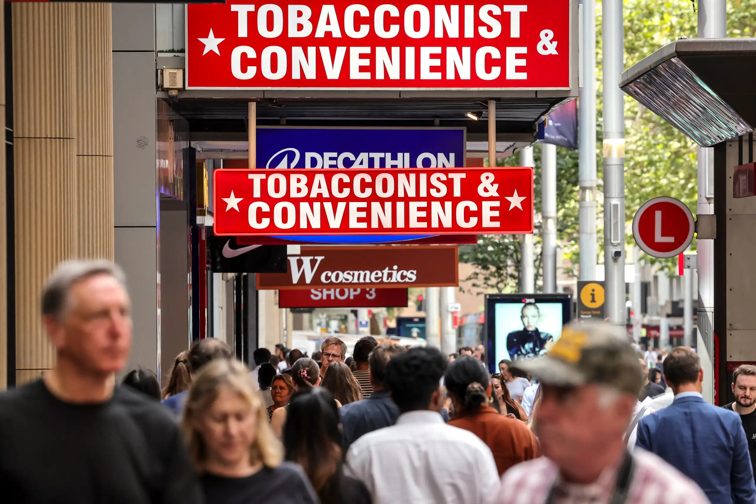 People walk past several tobacco shops on a busy city street.