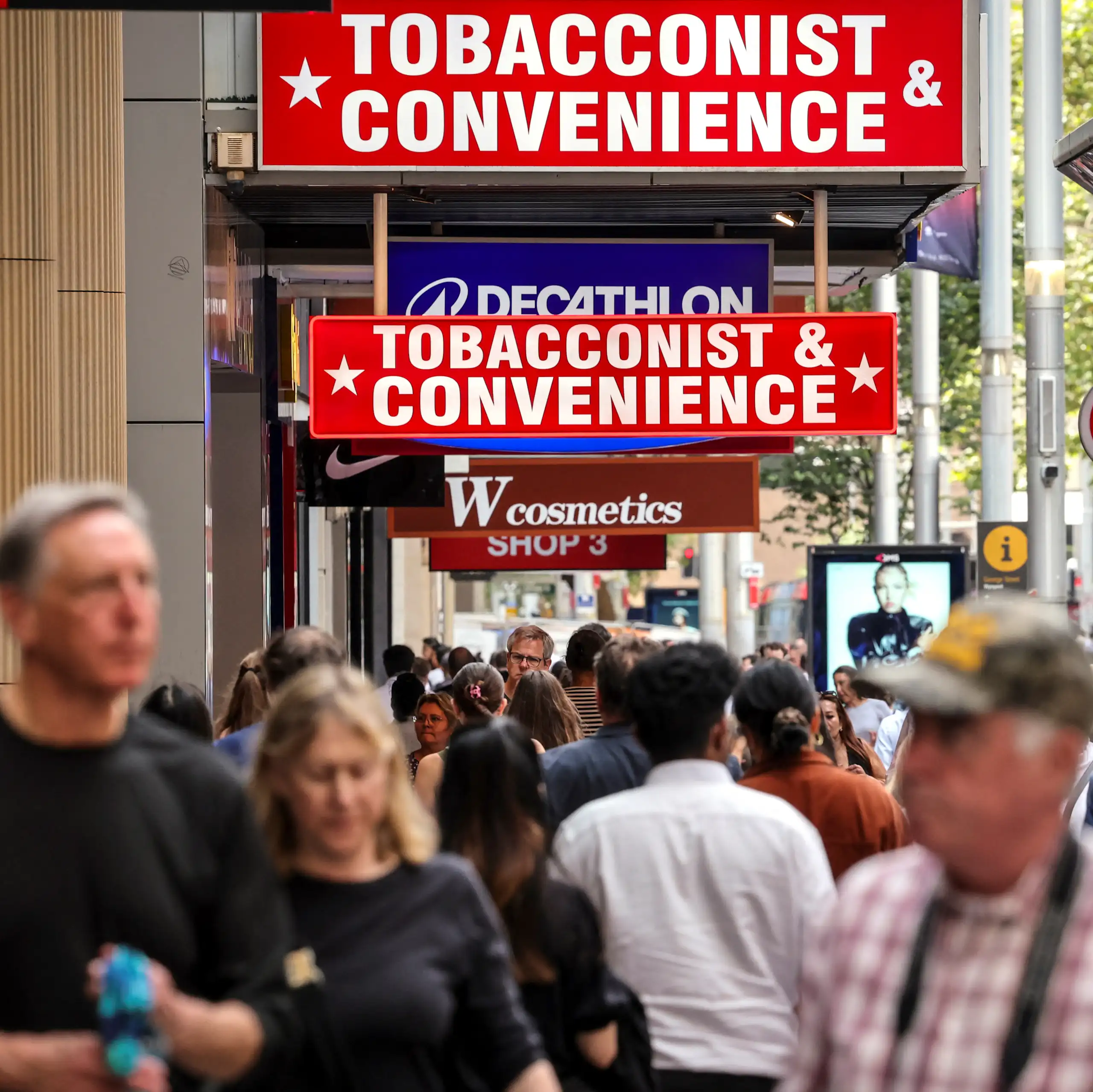 People walk past several tobacco shops on a busy city street.