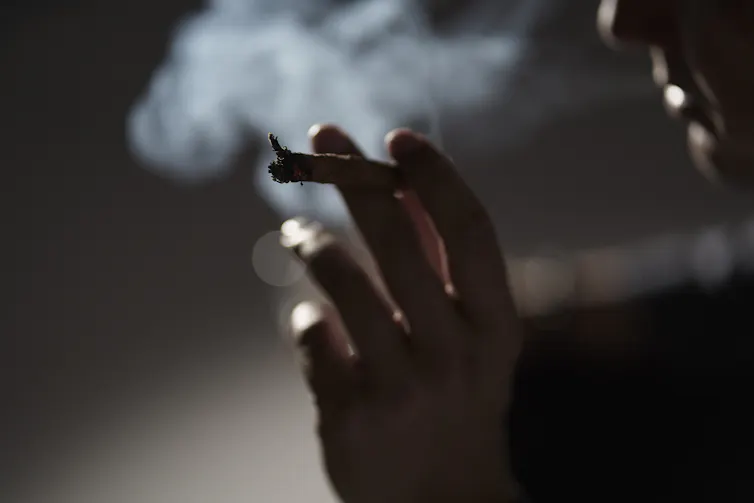 Close-up of a hand holding a cigarette, with the cigarette user exhaling smoke.