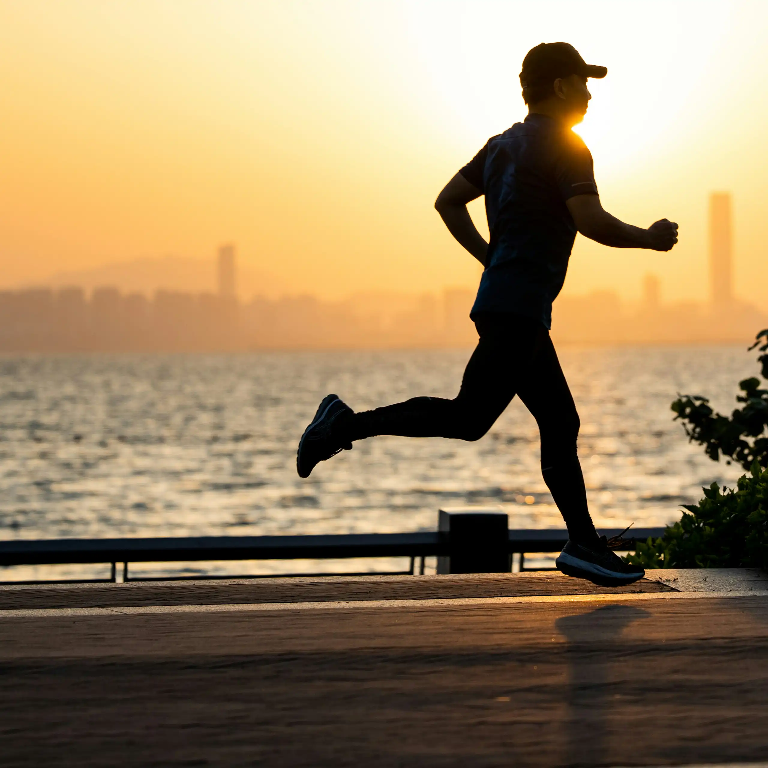 Man runs along harbour at sunset.