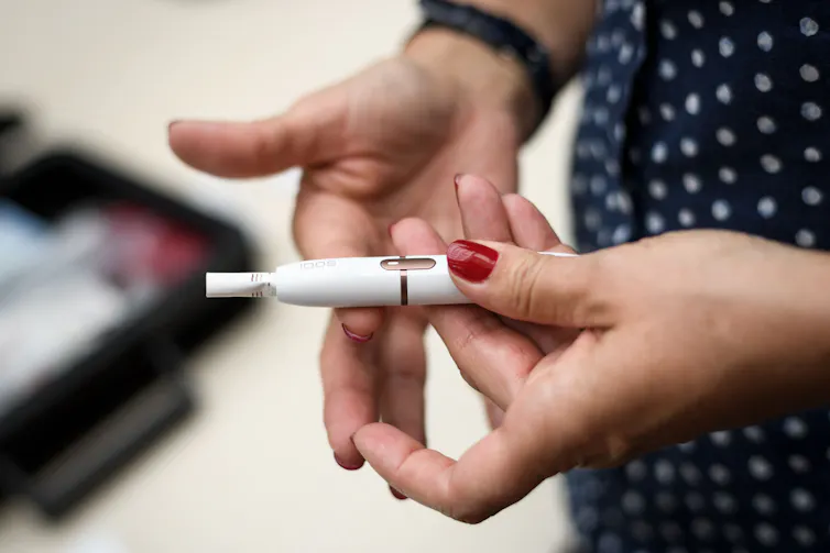 A woman's hand holds an electronic device with a cigarette coming out of it.