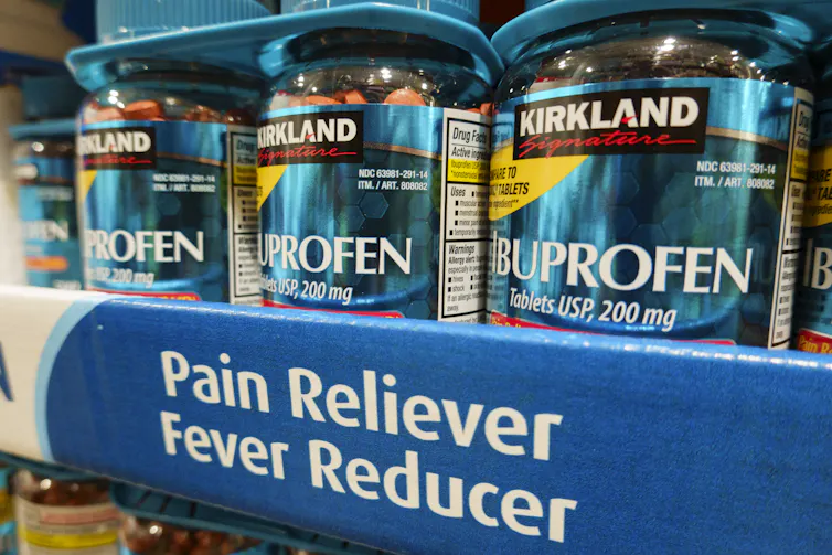 A shelf displaying bottles of ibuprofen, which are clear and full of small, circular pills