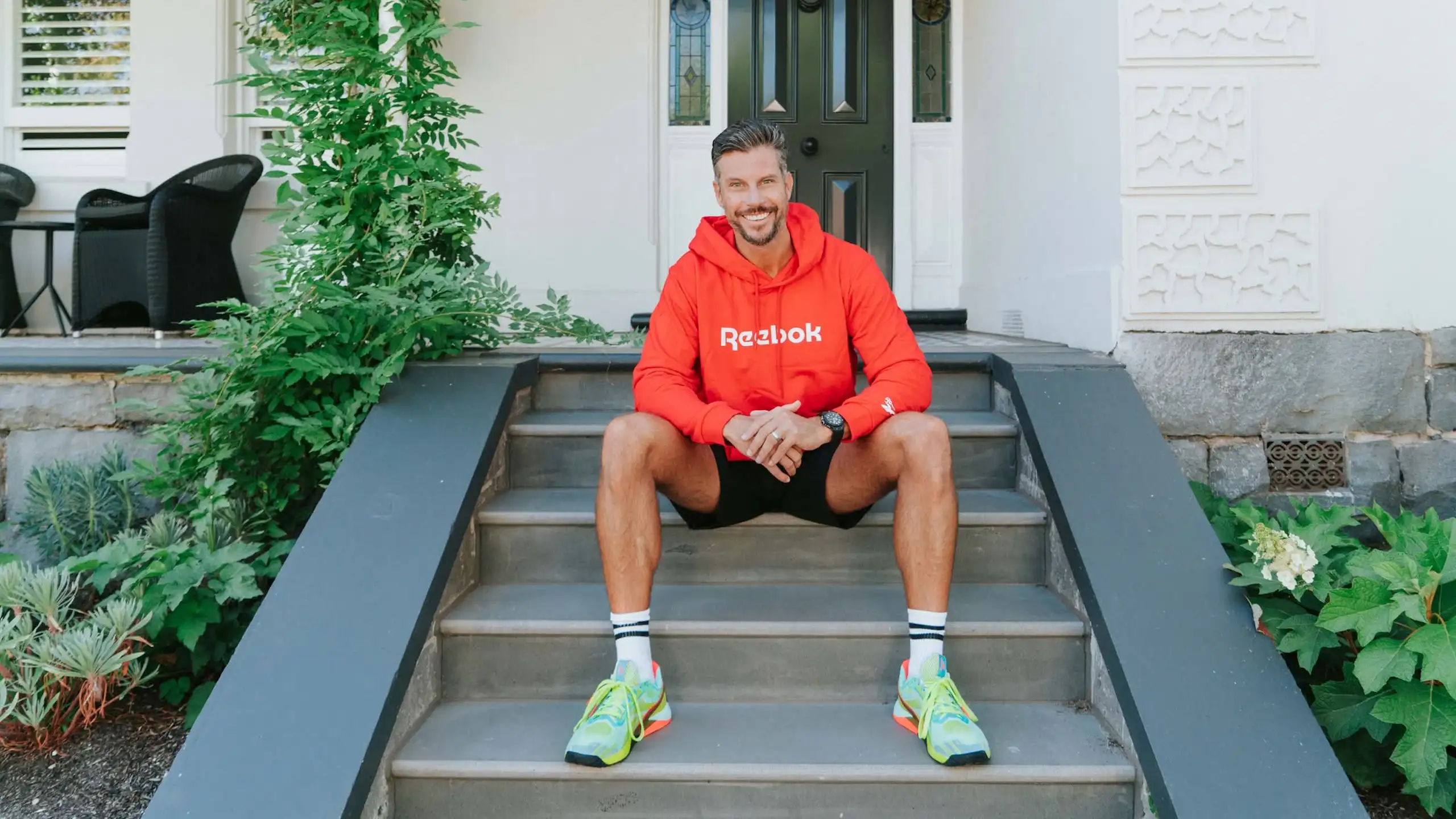 A man in workout clothes sits on the front steps of a house