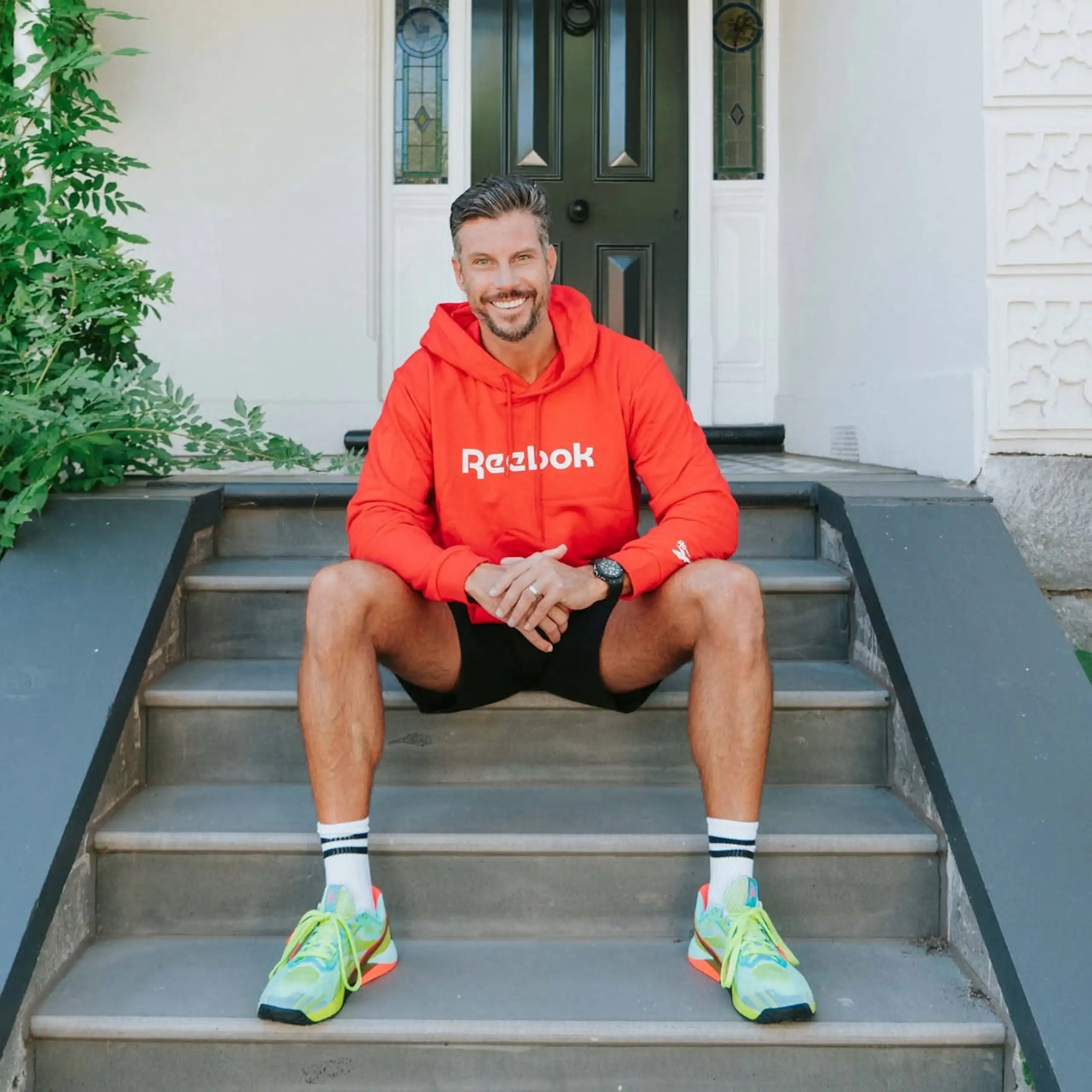 A man in workout clothes sits on the front steps of a house