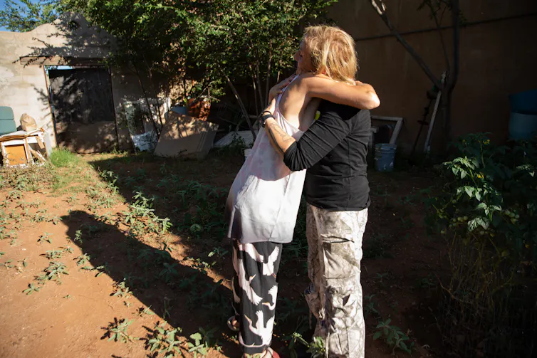 Two women hugging in a rural yard.