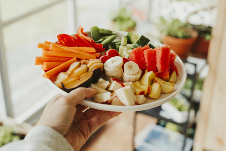 Hand holds a plate of chopped bananas, carrot, watermelon and other fruit and veg.