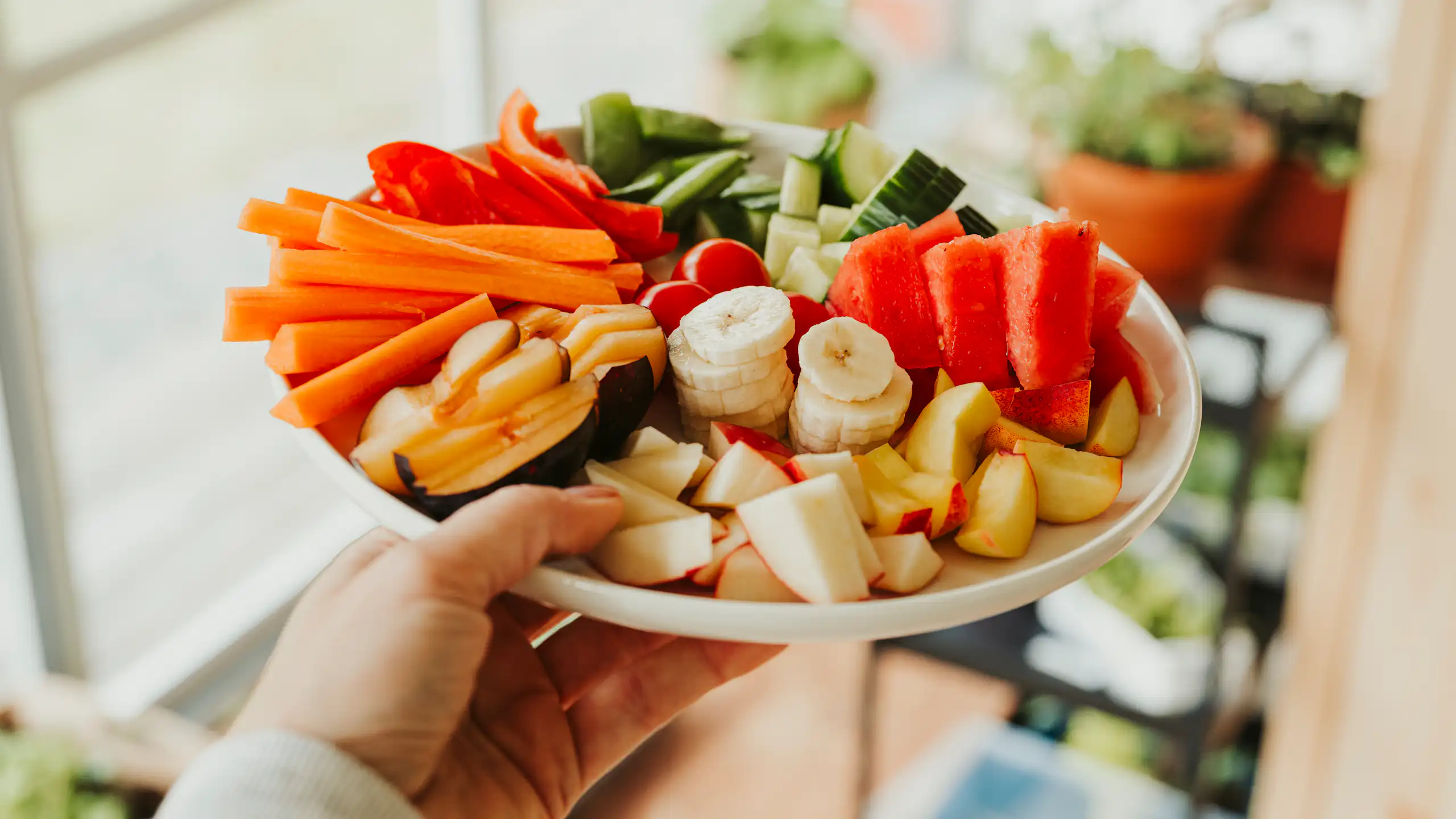 Hand holds a plate of chopped bananas, carrot, watermelon and other fruit and veg.