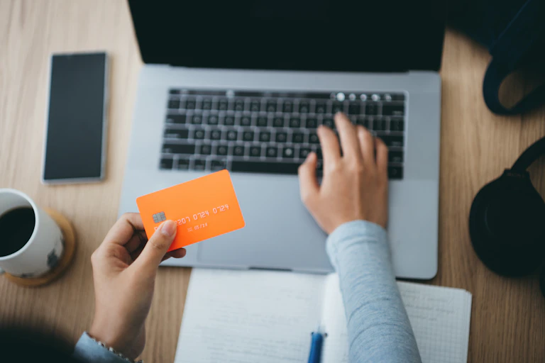 A woman holds a credit card over a laptop keyboard while typing with the other hand.