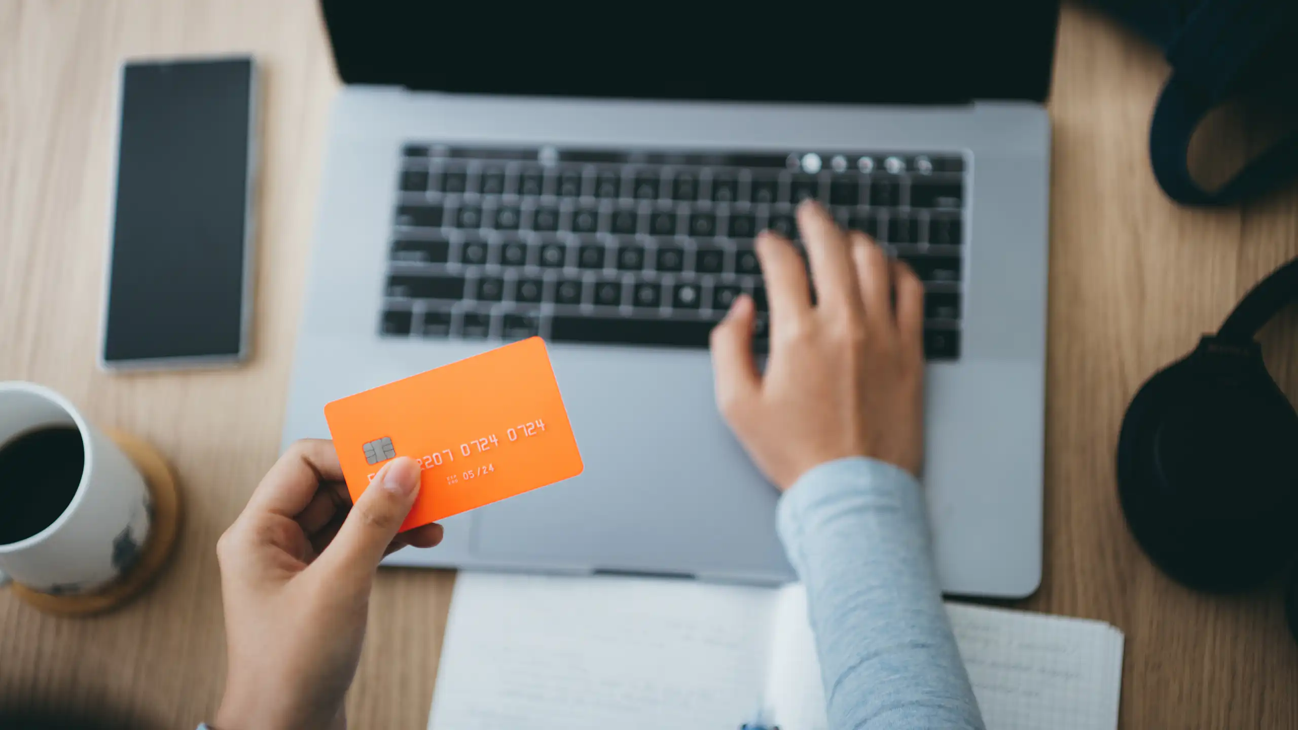 A woman holds a credit card over a laptop keyboard while typing with the other hand.