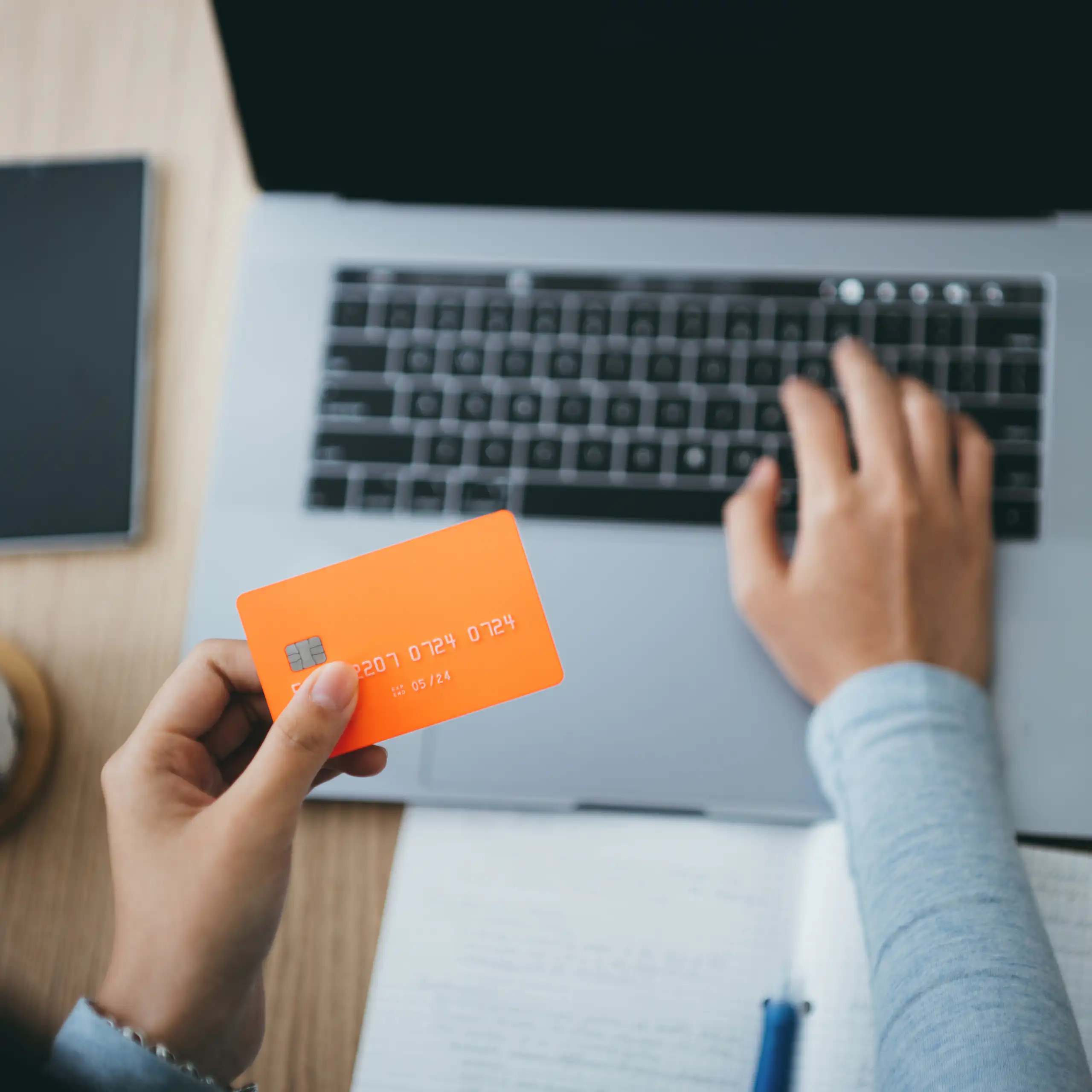 A woman holds a credit card over a laptop keyboard while typing with the other hand.