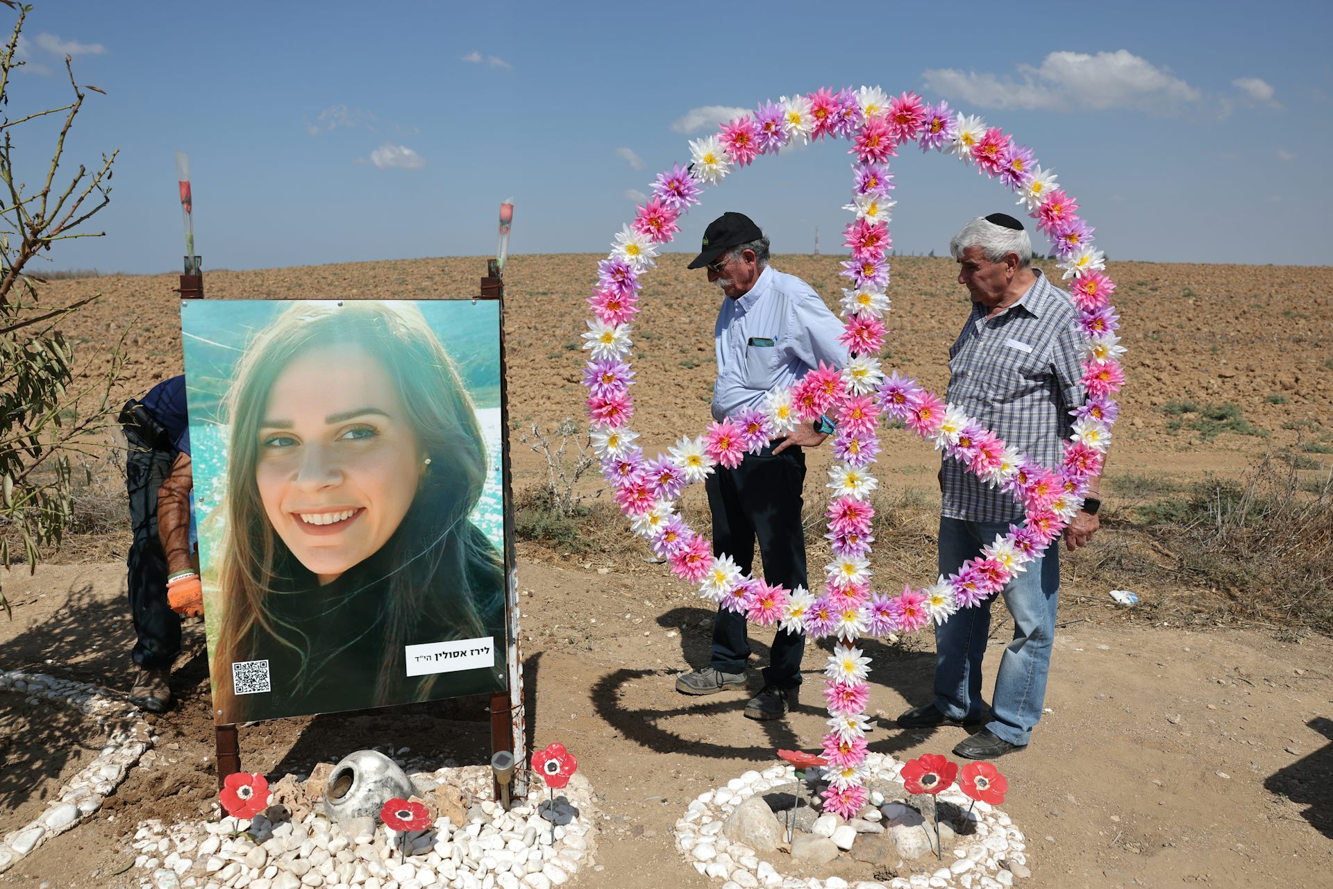 An old man and a young man look at the image of a young woman. In the foregrond is a decorated peace sign.