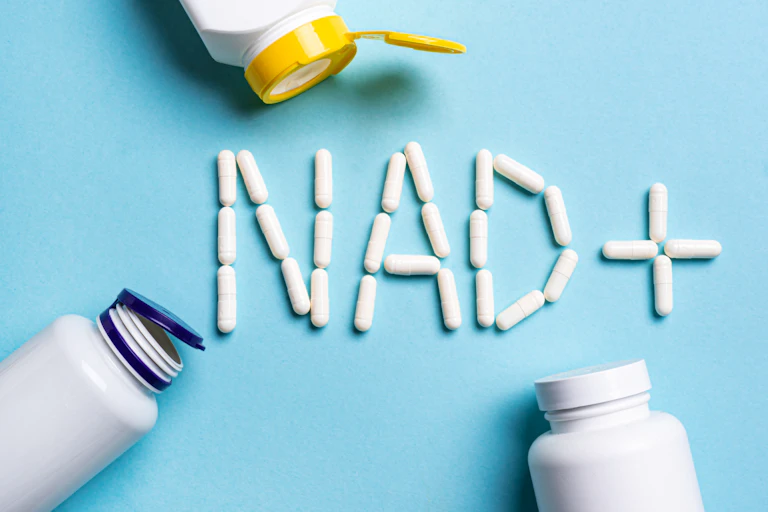 Top view of three open supplement containers and NAD+ supplement pills arranged to spell out 'NAD+' on blue background