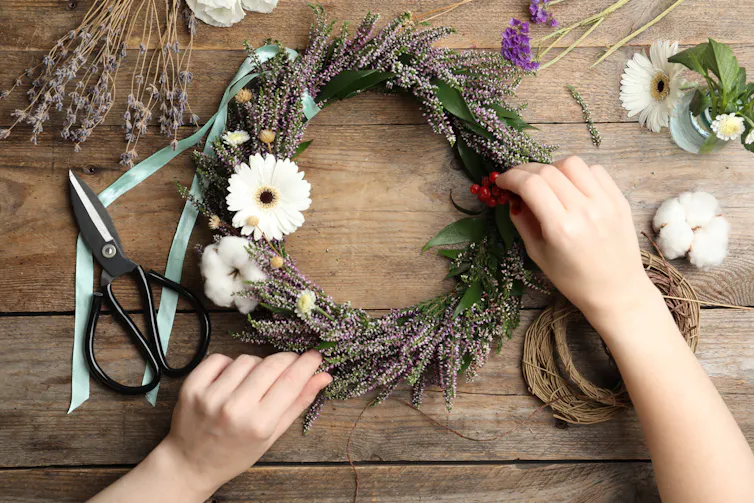 hands making autumnal floral wreath with scissors and ribbon laid out on wooden table