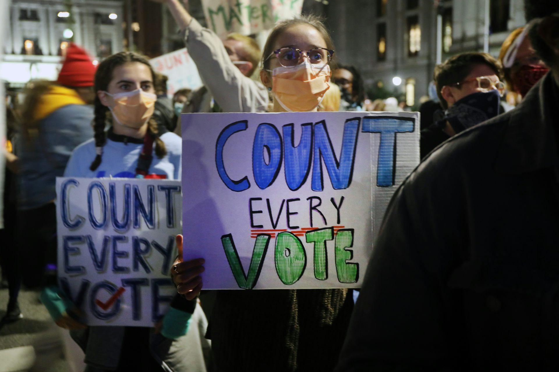 Protesters outside wearing masks hold signs that say 'Count every vote'