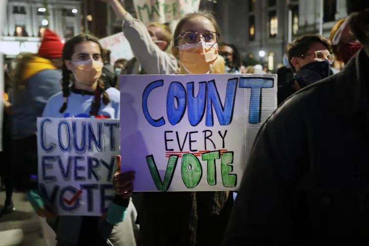 Protesters outside wearing masks hold signs that say 'Count every vote'