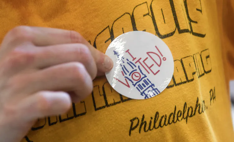 Person wearing yellow T-shirt places sticker that says 'I Voted' on their chest