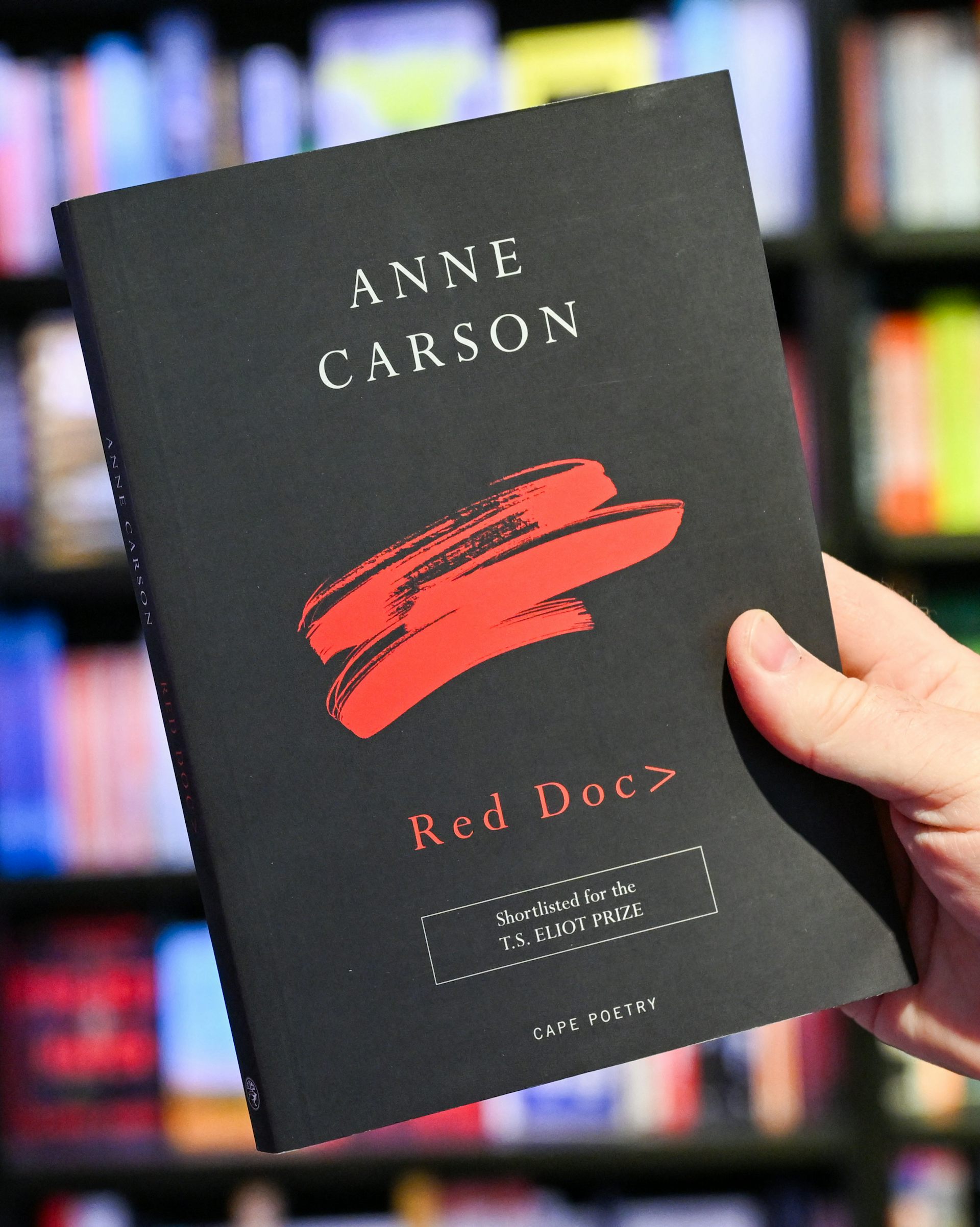 A hand holding a black book with red lettering.