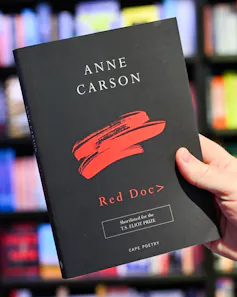 A hand holding a black book with red lettering.