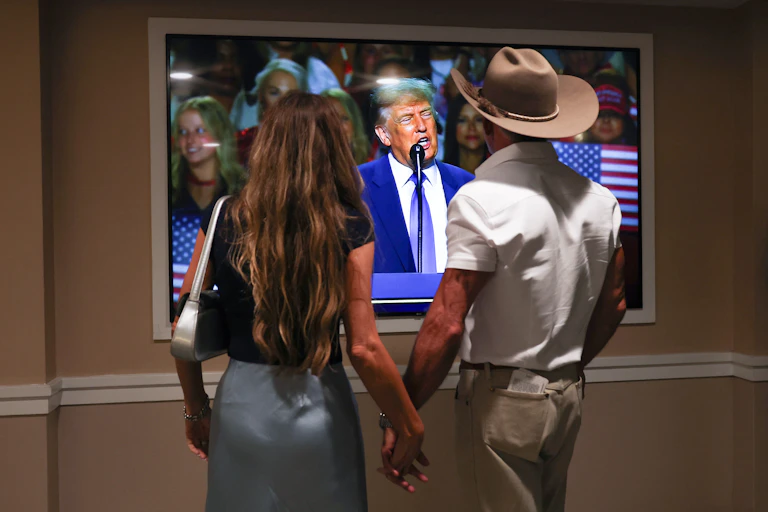 un couple regarde un écran retransmettant le discours de Trump.