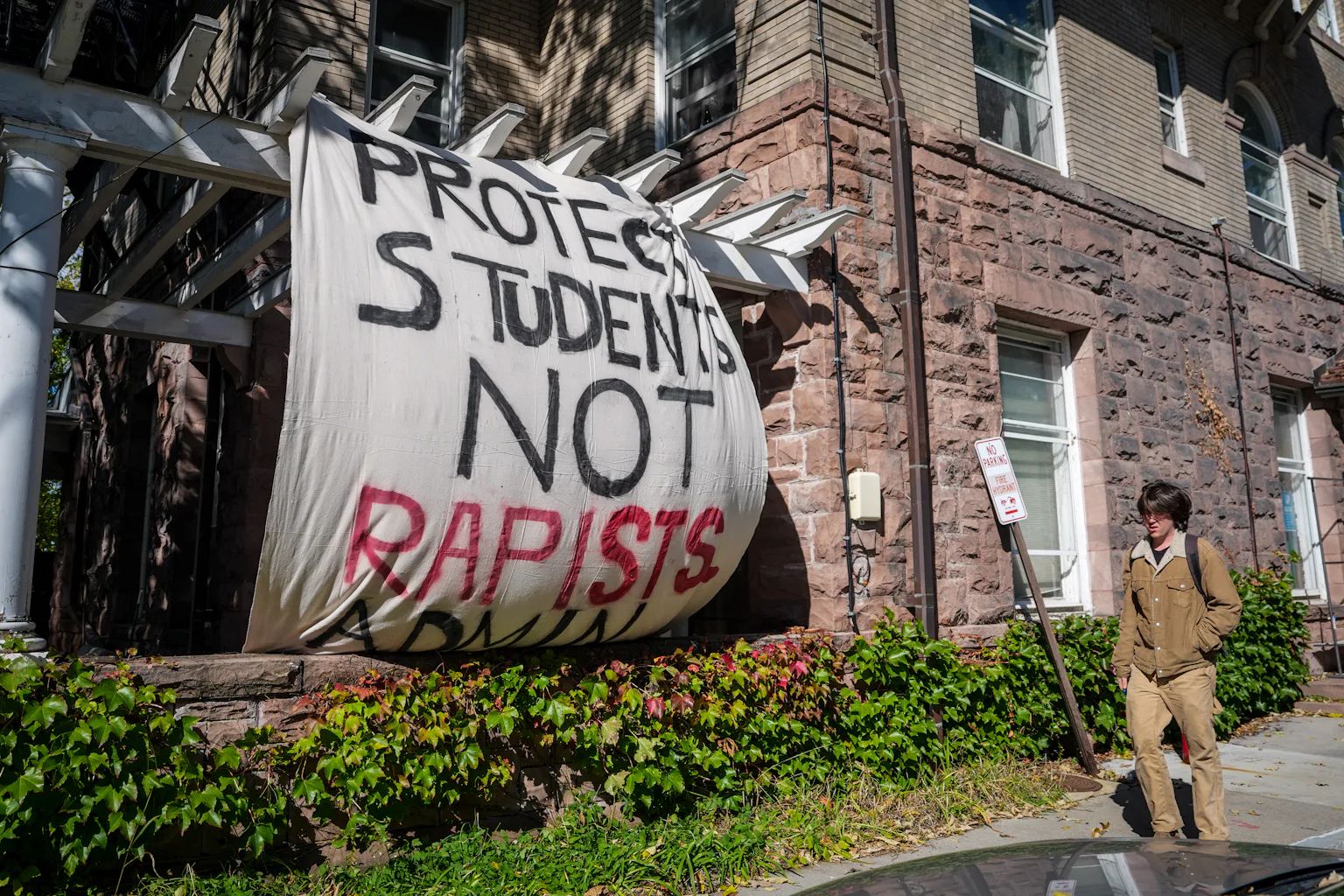 A Banner saying 'Protect students, not rapists" hangs on the outside of a stone college building