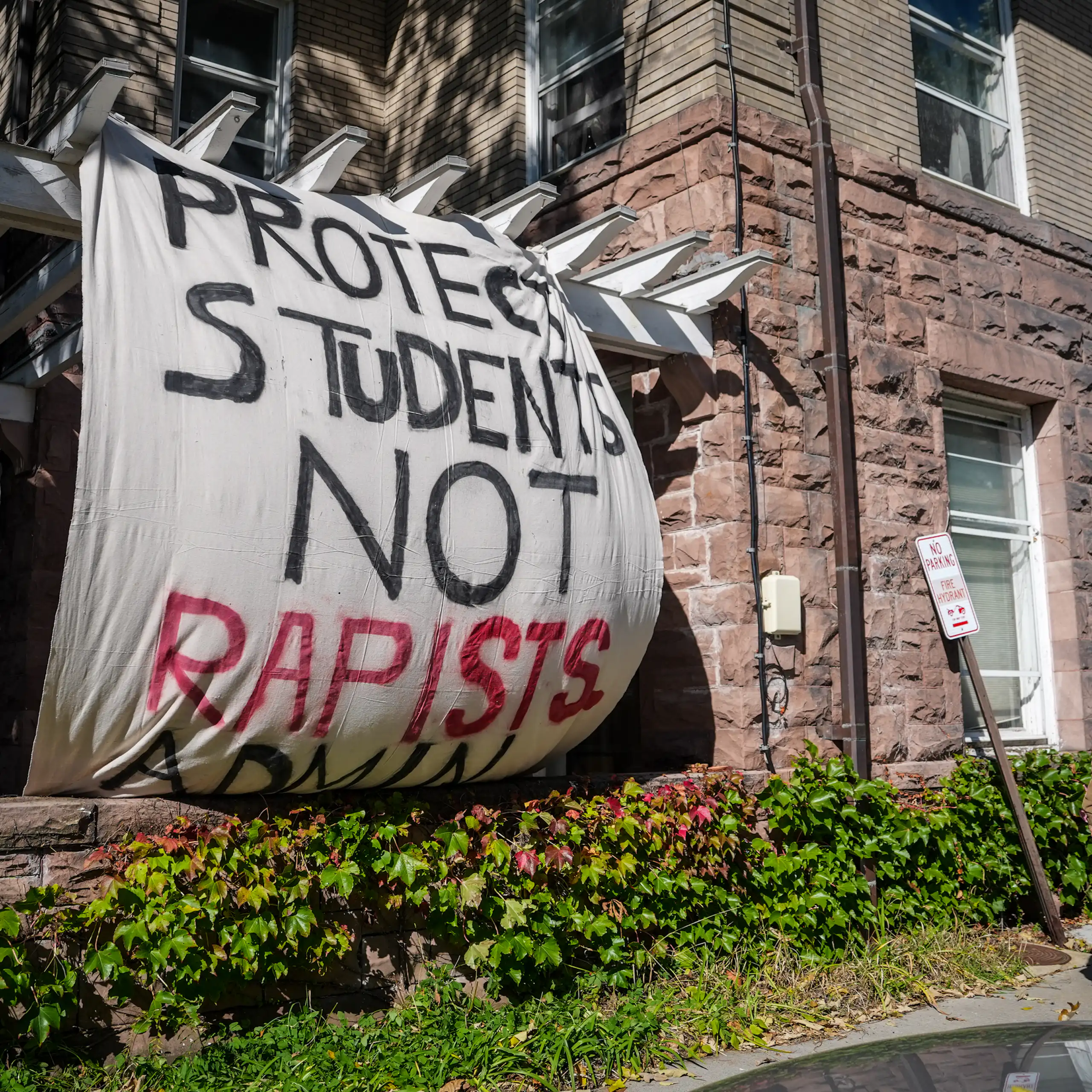 A Banner saying 'Protect students, not rapists" hangs on the outside of a stone college building