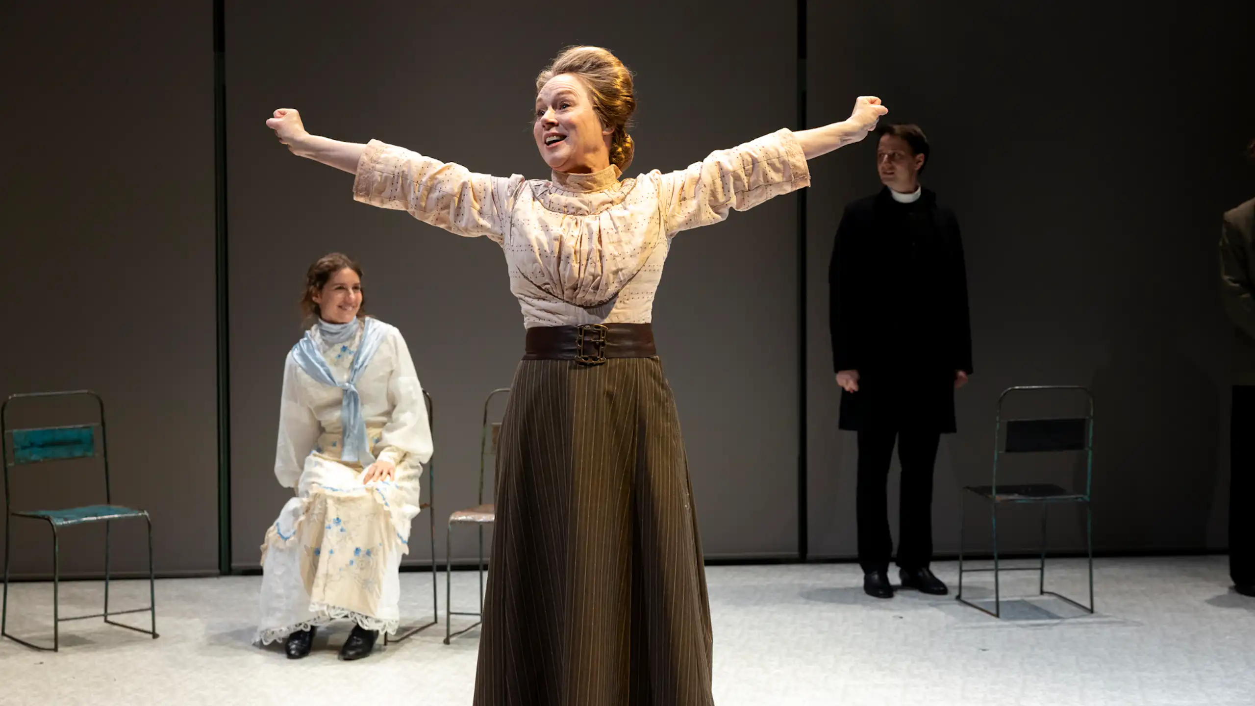 Production image: a woman stands, joyous, with her hands outstretched.
