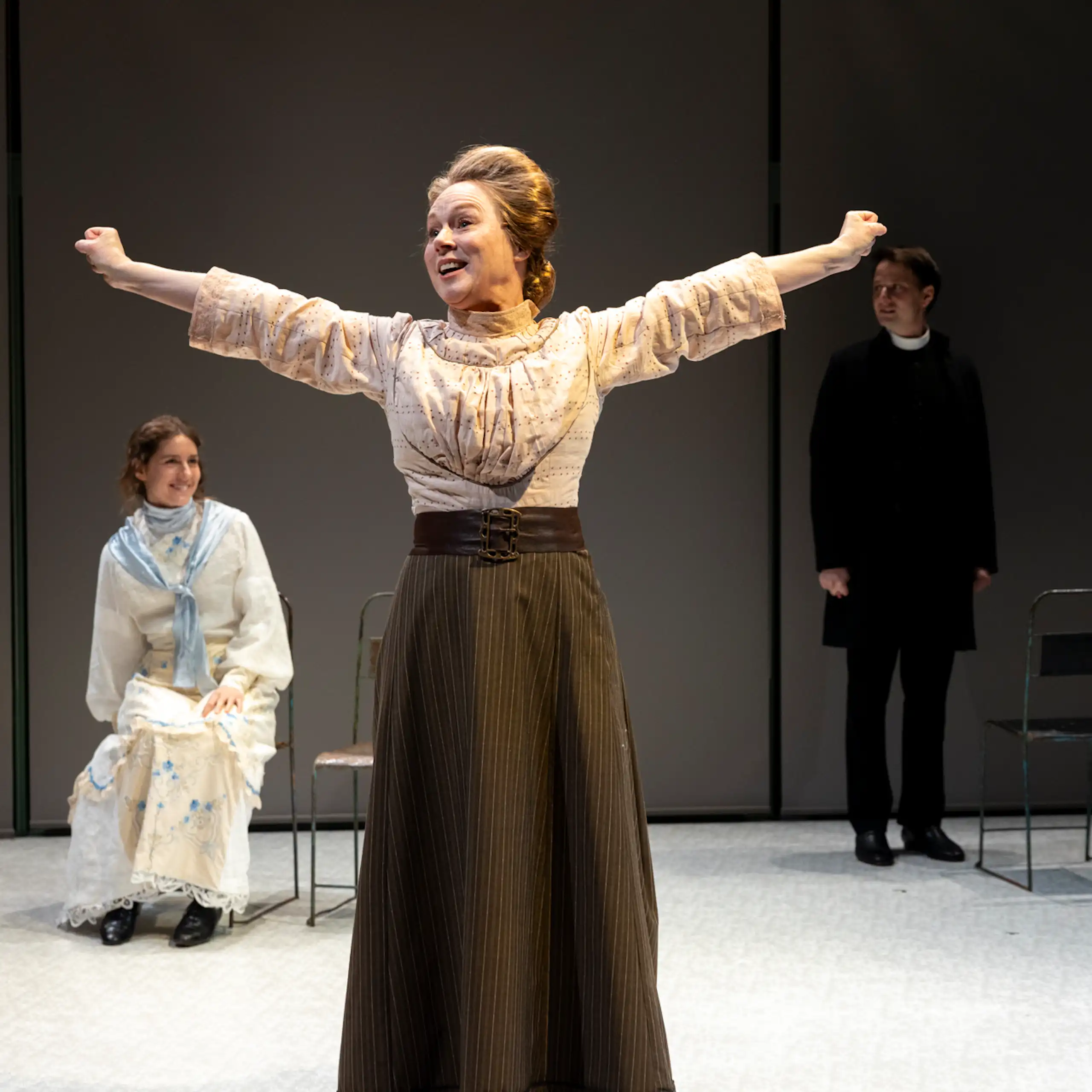 Production image: a woman stands, joyous, with her hands outstretched.
