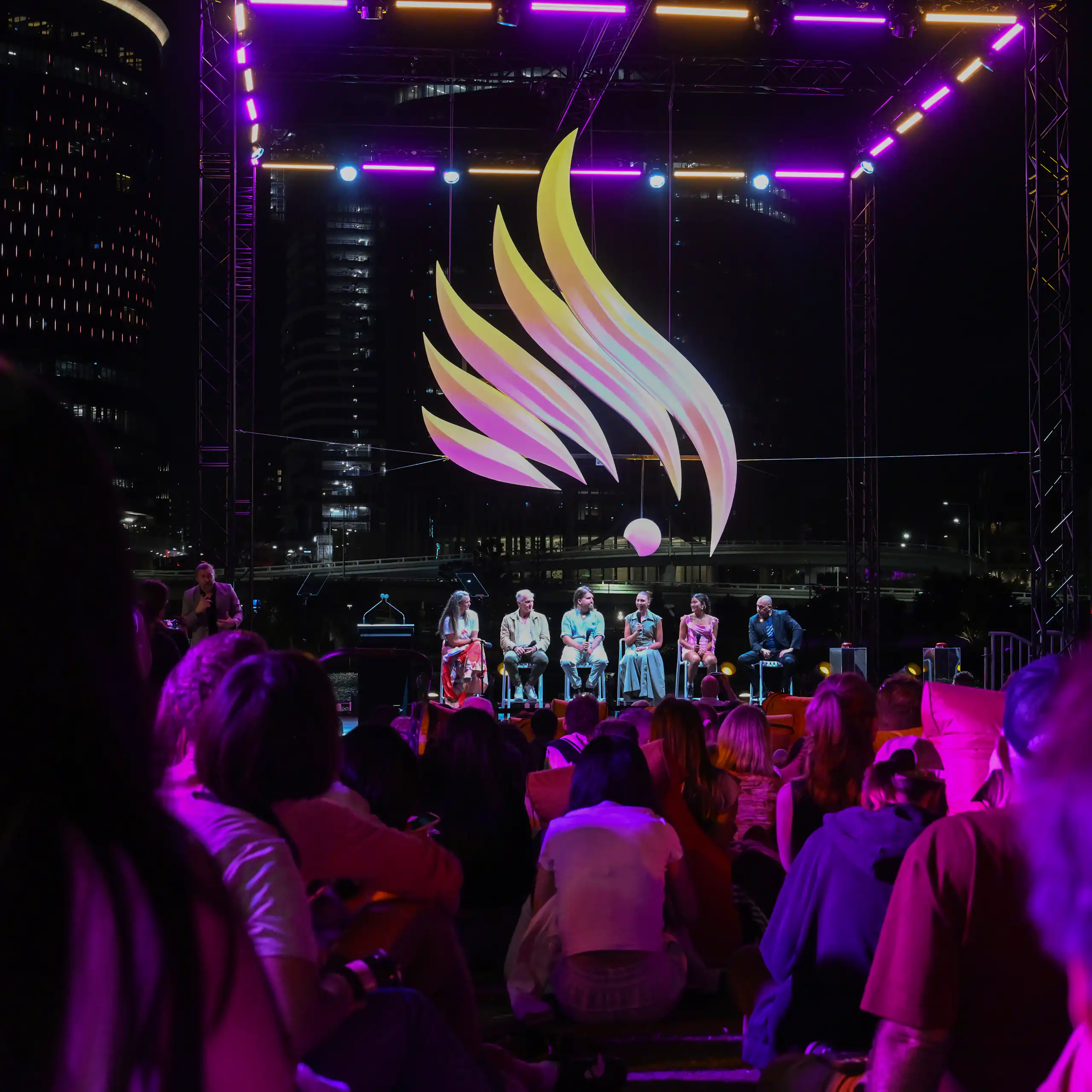 Crowds of people attend an emblem reveal event at night.