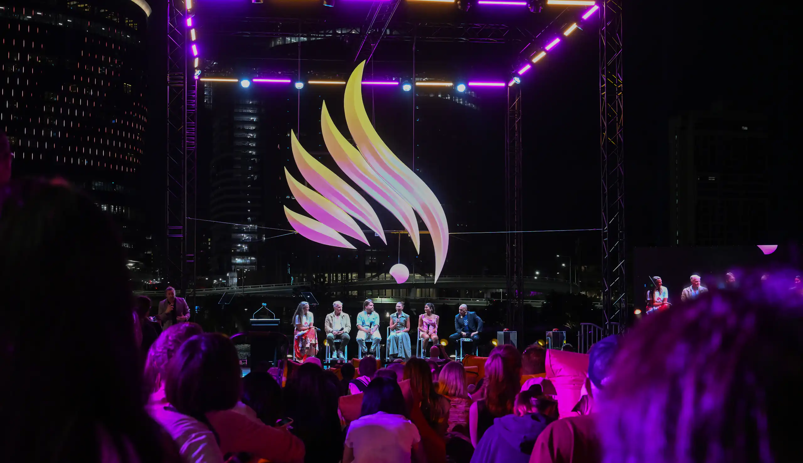 Crowds of people attend an emblem reveal event at night.