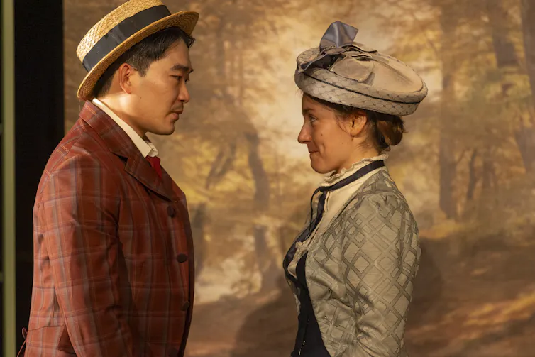 Production image: a man and a woman coyly smile at each other.