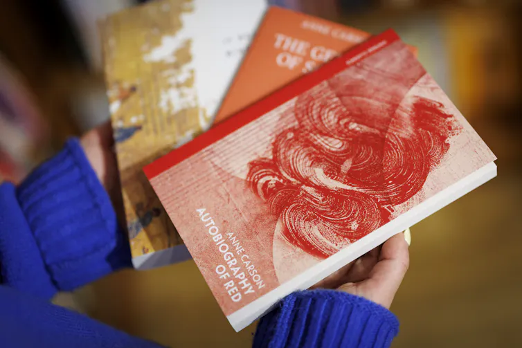 two hands holding three books by Anne Carson, with Autobiography of Red at the top