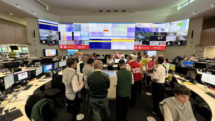 A group of people gather in a room to discuss bushfire management, surrounded by screens full of information.
