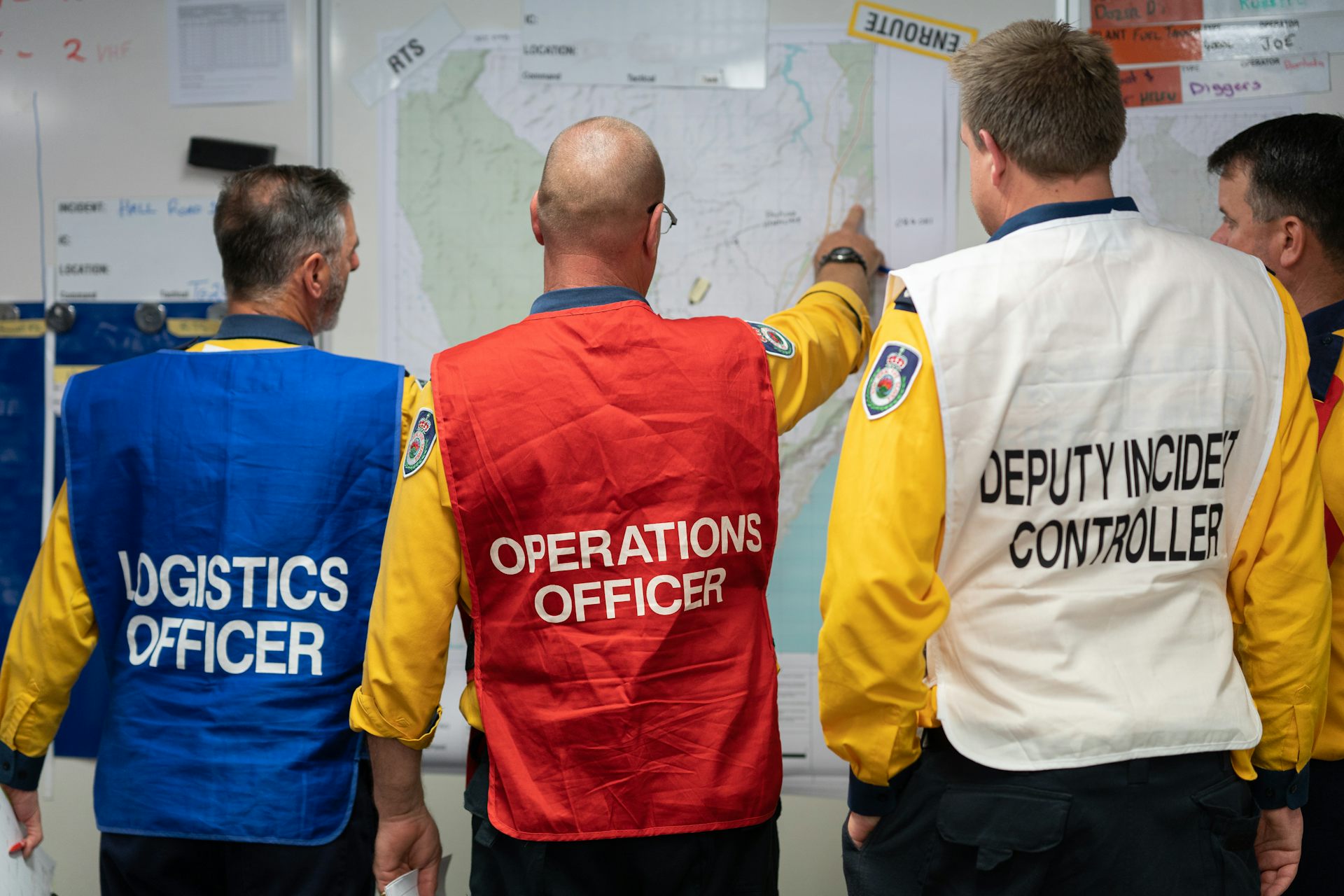 Four men from a fire agency discuss plans while looking at a whiteboard.