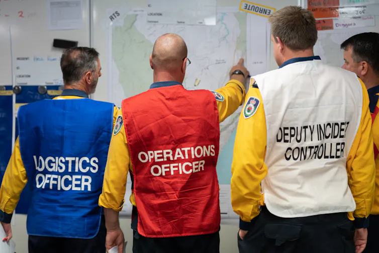 Four men from a fire agency discuss plans while looking at a whiteboard.