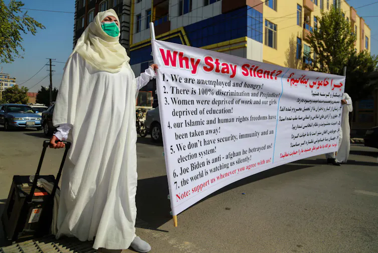 A university teacher and member of her family hold a protest banner and wear shrouds that Muslims put on a body before burial, during a 2021 protest in Kabul.