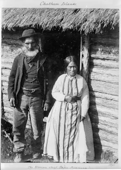 Black and white image of Tapu Hirawana Maitarawai and his wife Rohana in front of thatched cottage.