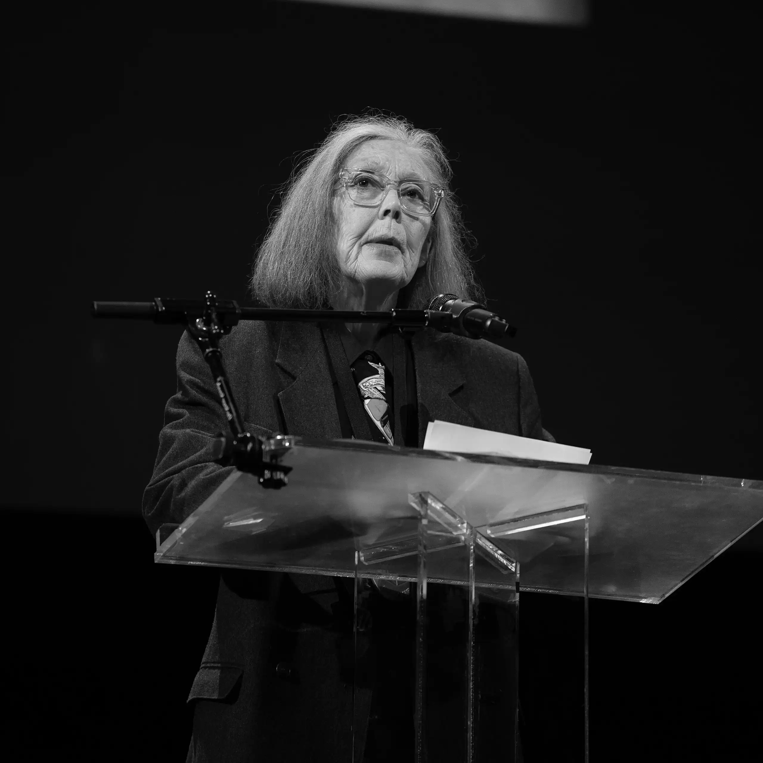 Fotografía en blanco y negro de una mujer de pelo blanco leyendo delante de un atril.