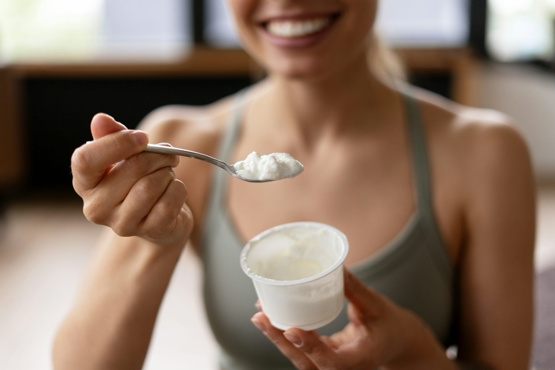 A woman wearing workout clothes holds and cup and a spoonful of yoghurt.